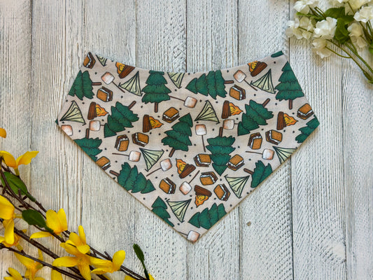 Pet bandana with camping-themed pattern on a wooden surface with flowers.