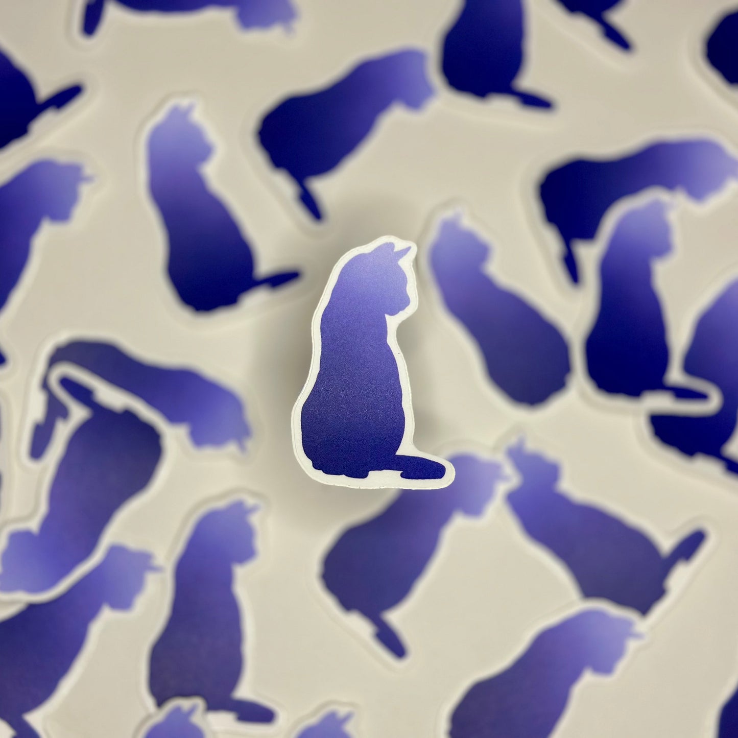 A blue vinyl sticker in the shape of a cat's silhouette, surrounded by other similar stickers in the background.