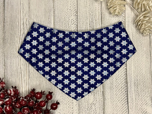 A blue bandana with silver Star of David patterns laid out on a wooden surface, with decorative red berries and white pinecones to the side.