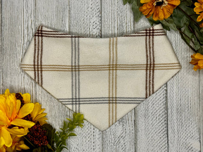 A medium-sized plaid flannel pet bandana with a scrunchie neck, displayed on a wooden background with fall flowers around it.