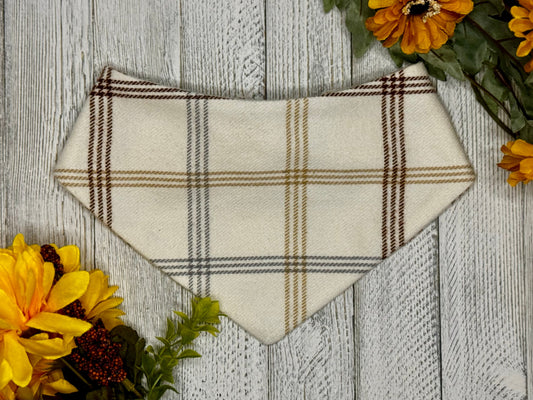 A medium-sized plaid flannel pet bandana with a scrunchie neck, displayed on a wooden background with fall flowers around it.
