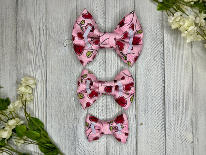 Picture of the backside of a pet bow tie showing the elastic straps that fit around a collar. Displayed on a wooden surface with flowers for decoration. 