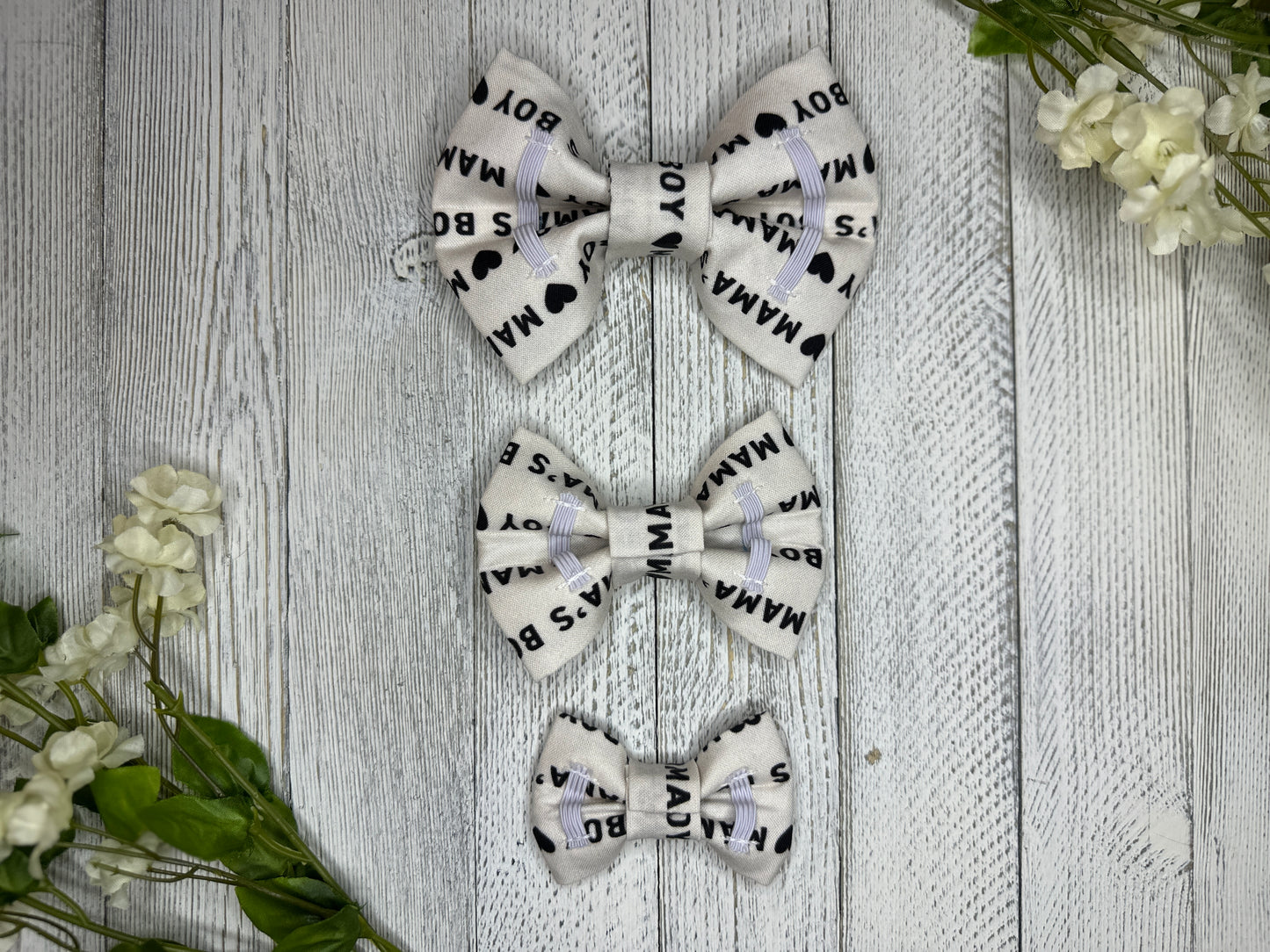 Picture of the backside of pet bow ties showing the elastic straps that fit around a collar. Displayed on a wooden surface with flowers for decoration. 