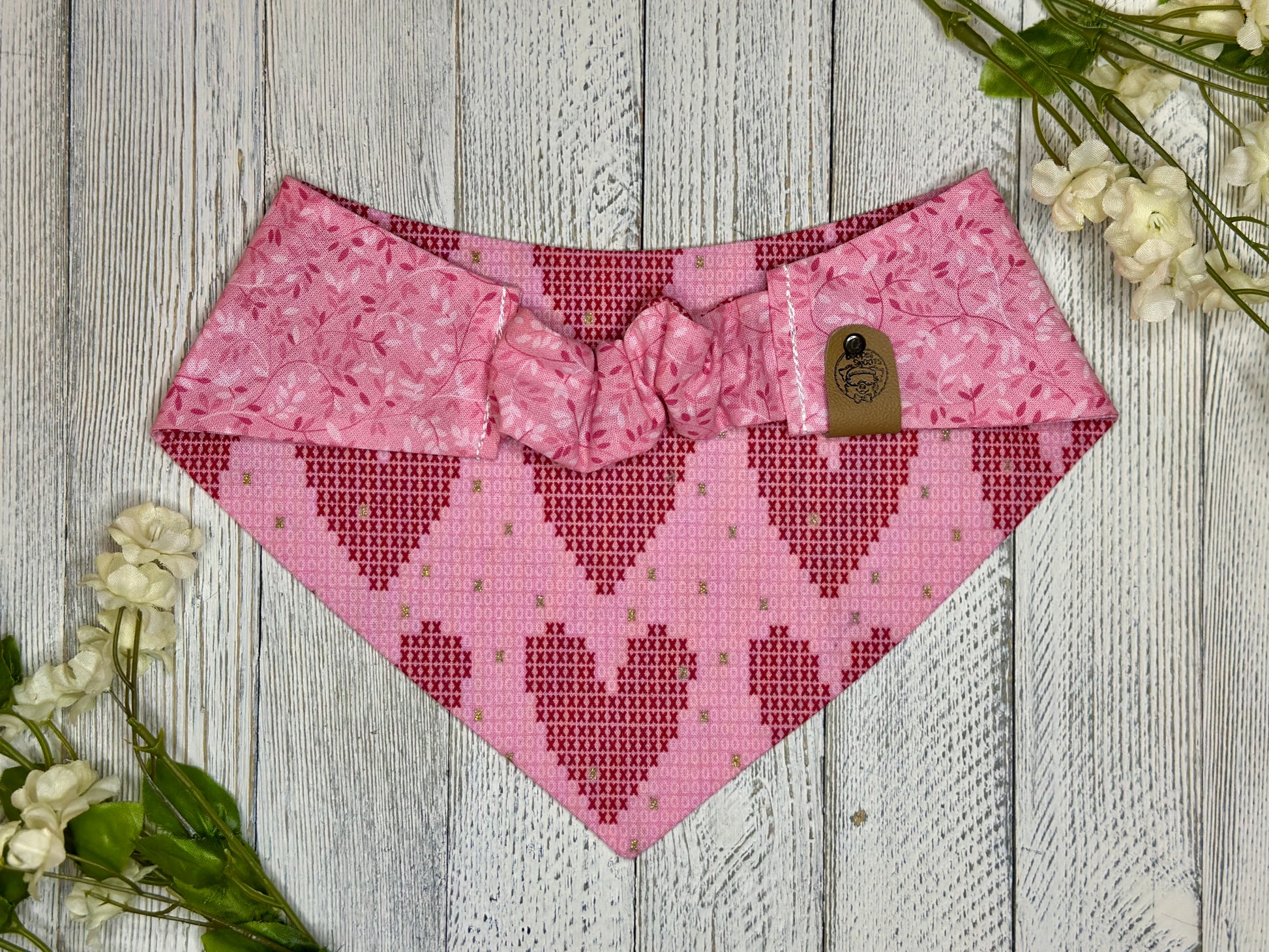 Picture of the backside of a pet bandana showing the scrunchie neckline. Displayed on a wooden surface with flowers for decoration. 