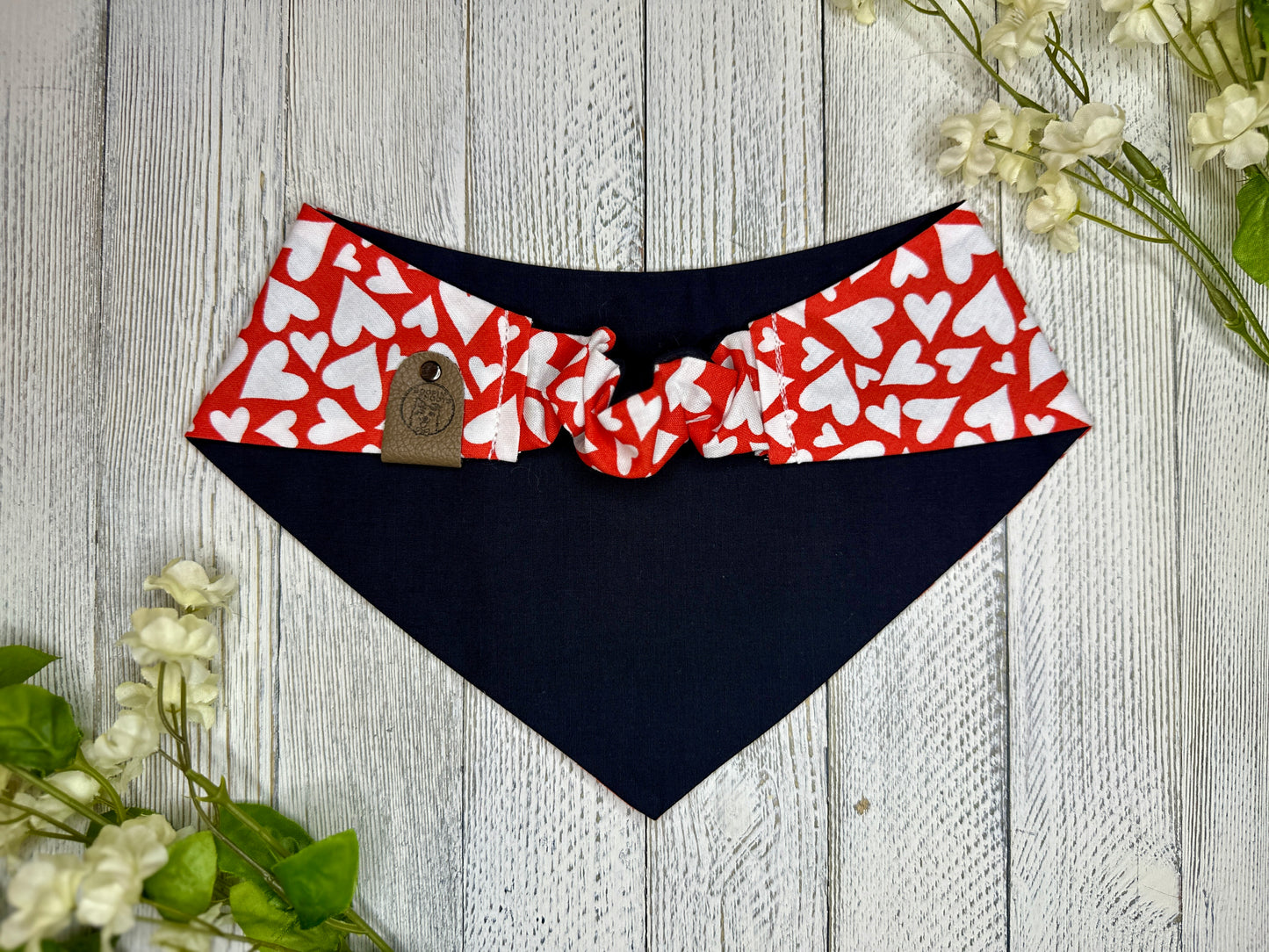 Picture of the backside of a pet bandana showing the scrunchie neckline. Displayed on a wooden surface with flowers for decoration.