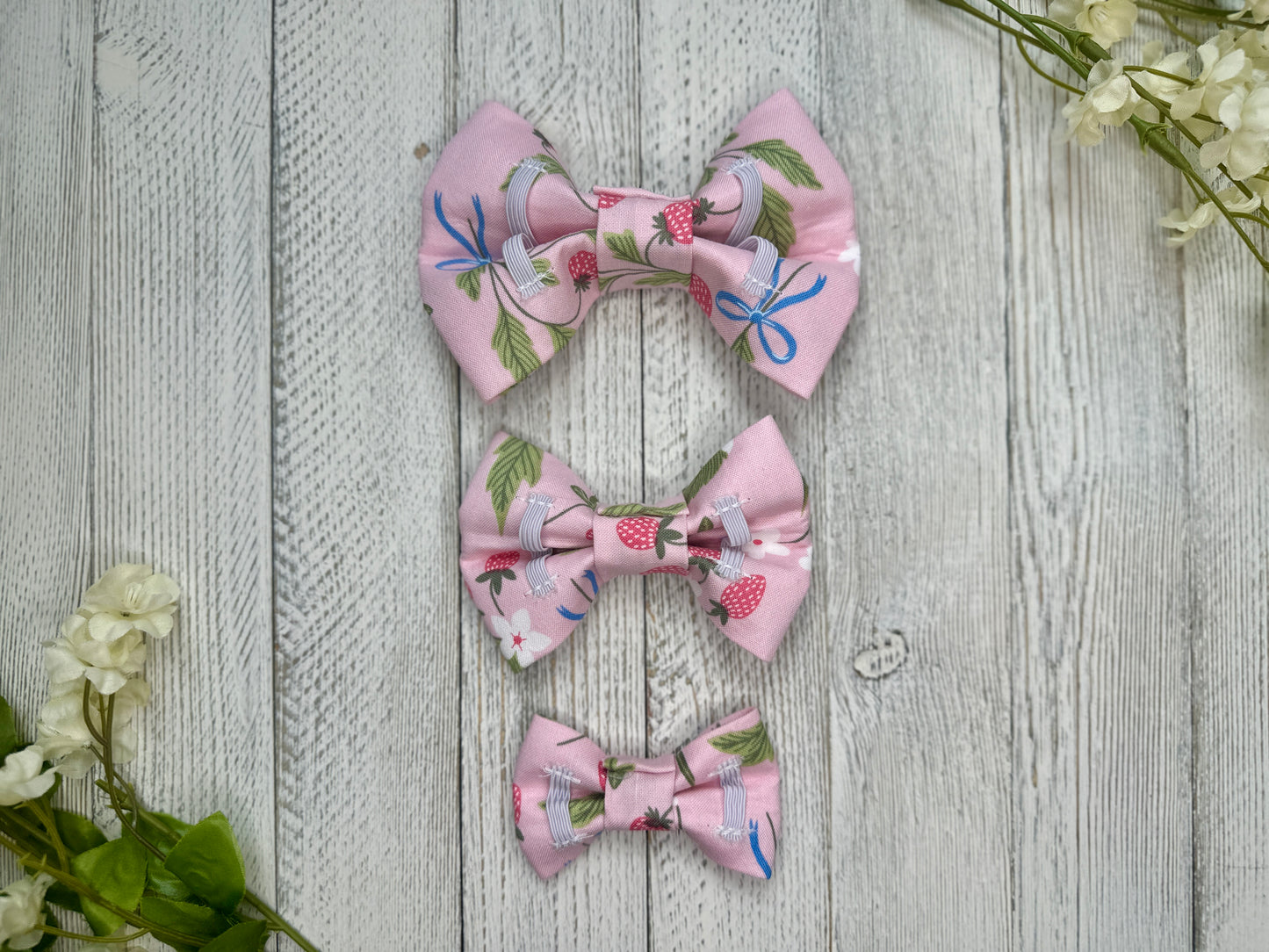 Picture of the backside of pet bow ties showing the elastic straps that fit around a collar. Displayed on a wooden surface with flowers for decoration. 