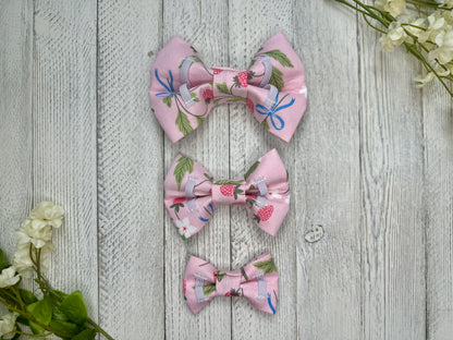 Picture of the backside of pet bow ties showing the elastic straps that fit around a collar. Displayed on a wooden surface with flowers for decoration. 
