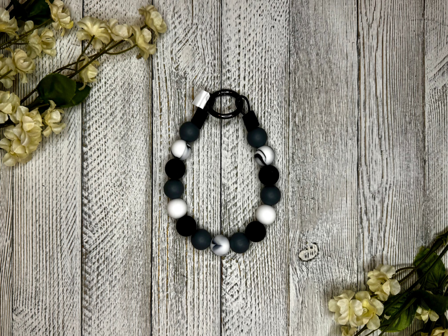 Beaded dog necklace with a black and white pattern including a marble effect Displayed on a wooden surface with flowers for decoration.