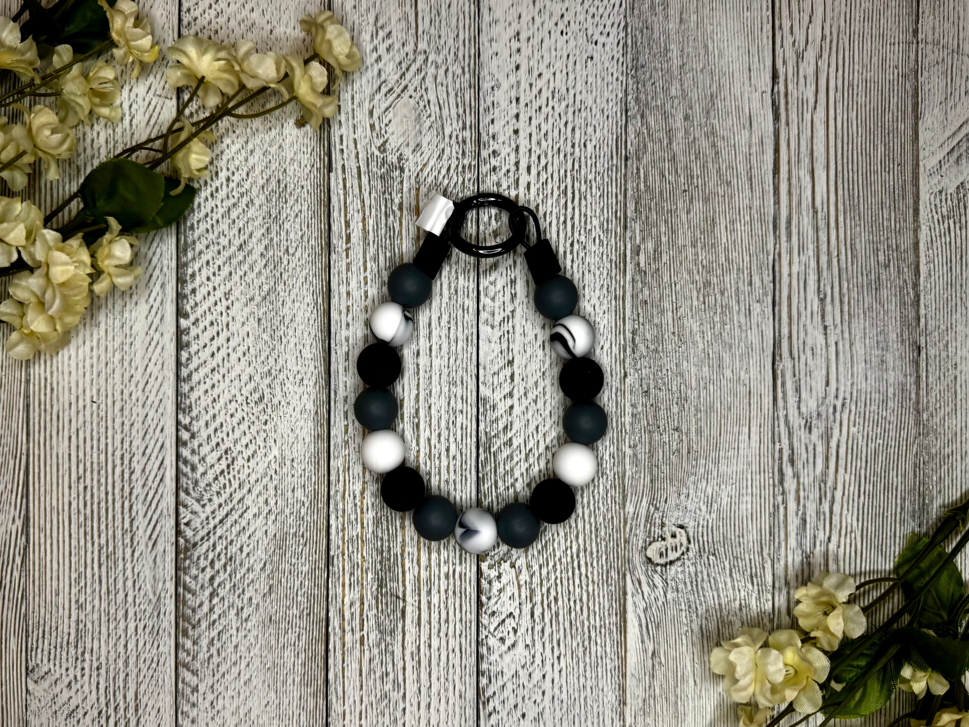 Beaded dog necklace with a black and white pattern including a marble effect Displayed on a wooden surface with flowers for decoration.