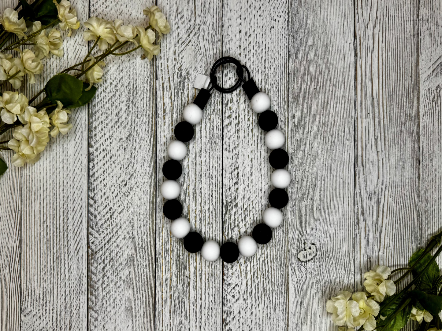 Beaded dog necklace with a black and white pattern. Displayed on a wooden surface with flowers for decoration.
