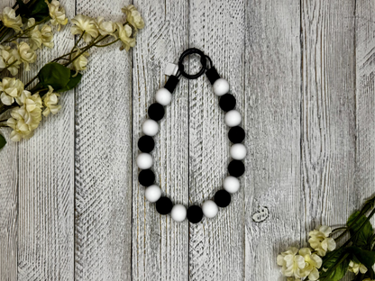 Beaded dog necklace with a black and white pattern. Displayed on a wooden surface with flowers for decoration.