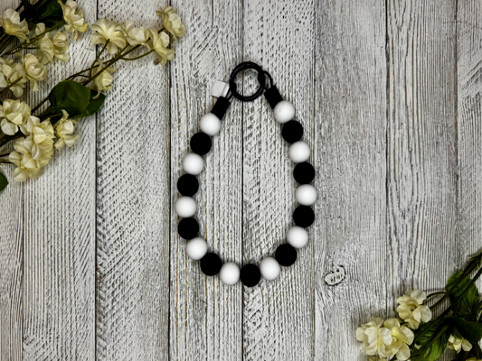 Beaded dog necklace with a black and white pattern. Displayed on a wooden surface with flowers for decoration.