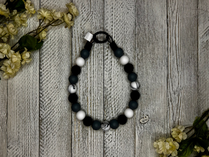 Beaded dog necklace with a black and white pattern including a marble effect. Displayed on a wooden surface with flowers for decoration.