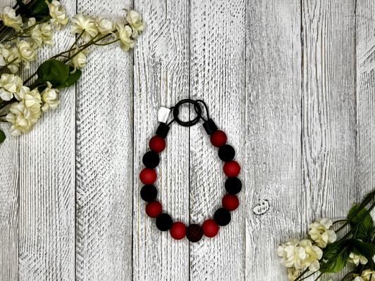 Beaded dog necklace with a red and black pattern including checkers. Displayed on a wooden surface with flowers for decoration.