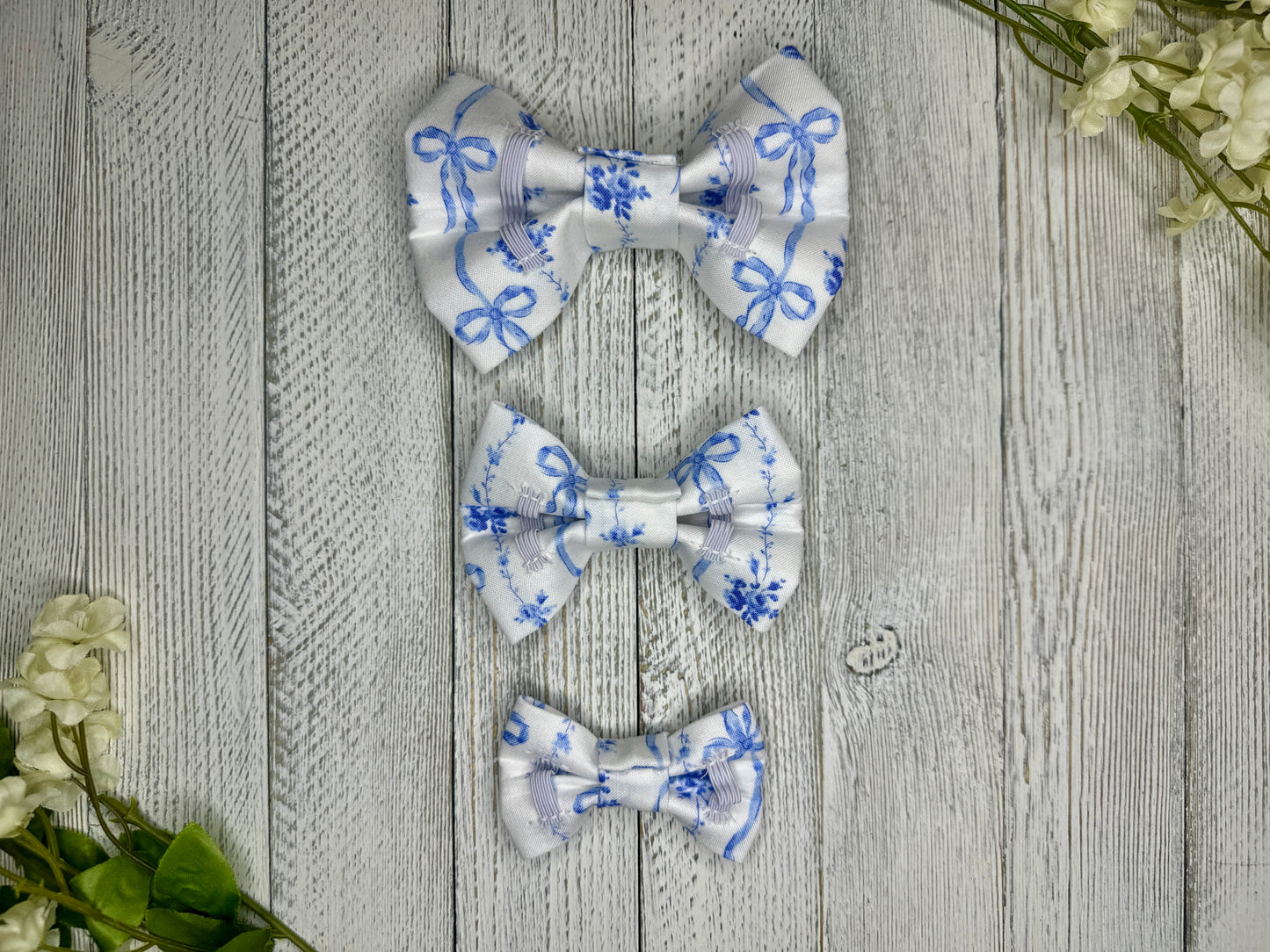 Picture of the backside of pet bow ties showing the elastic straps that fit around a collar. Displayed on a wooden surface with flowers for decoration.