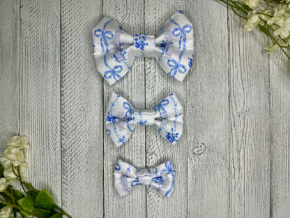 Picture of the backside of pet bow ties showing the elastic straps that fit around a collar. Displayed on a wooden surface with flowers for decoration.
