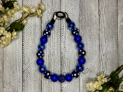 Beaded dog necklace with a blue and white pattern including polka dots. Displayed on a wooden surface with flowers for decoration.
