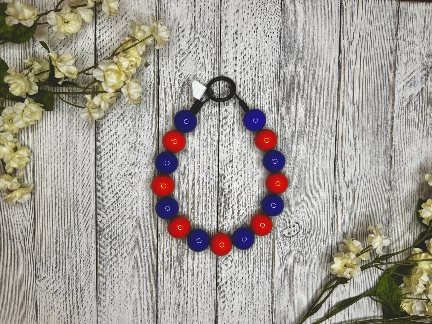 Beaded dog necklace with a blue and orange pattern. Displayed on a wooden surface with flowers for decoration.