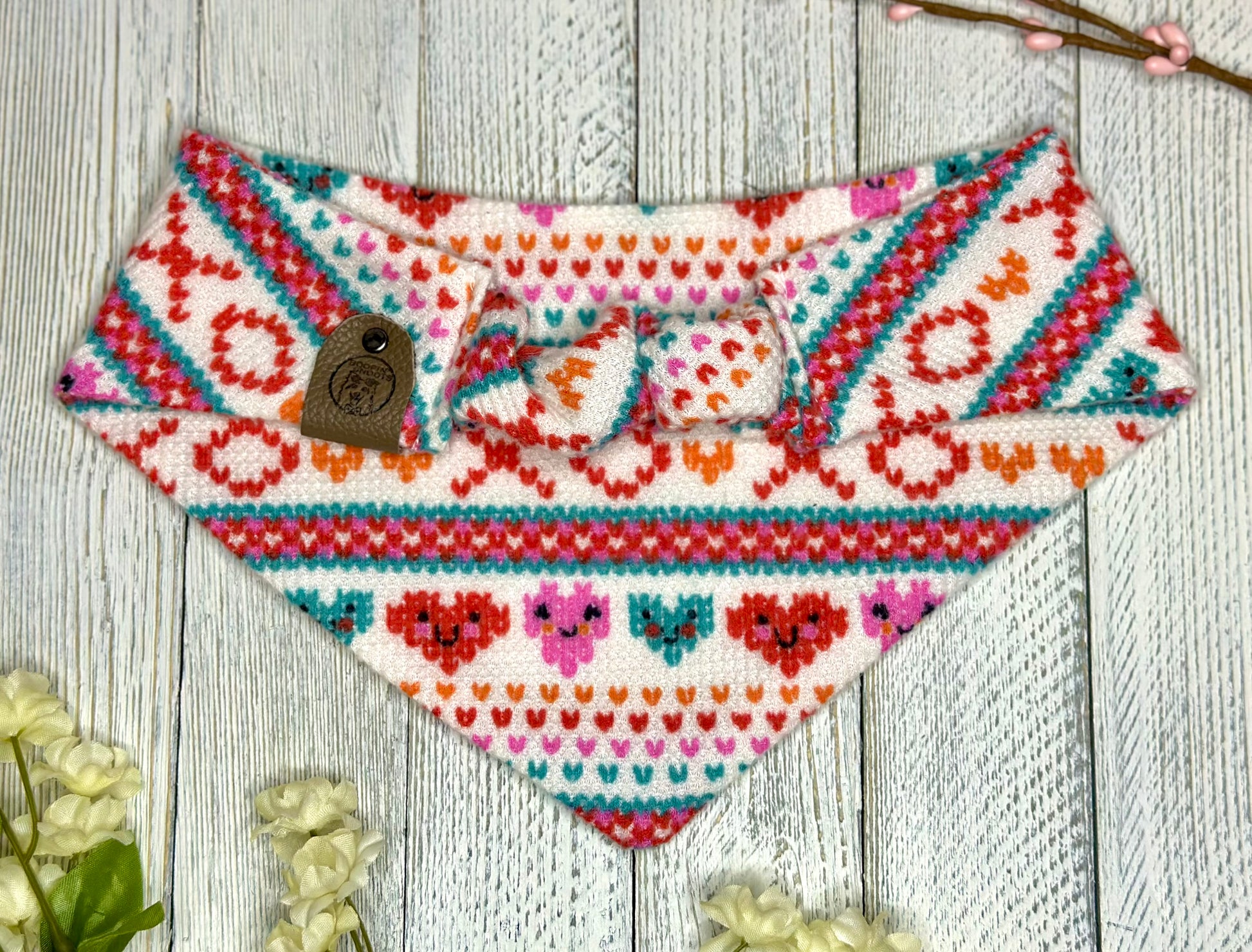 Picture of the backside of a pet bandana showing the scrunchie neckline. Displayed on a wooden surface with flowers for decoration. 