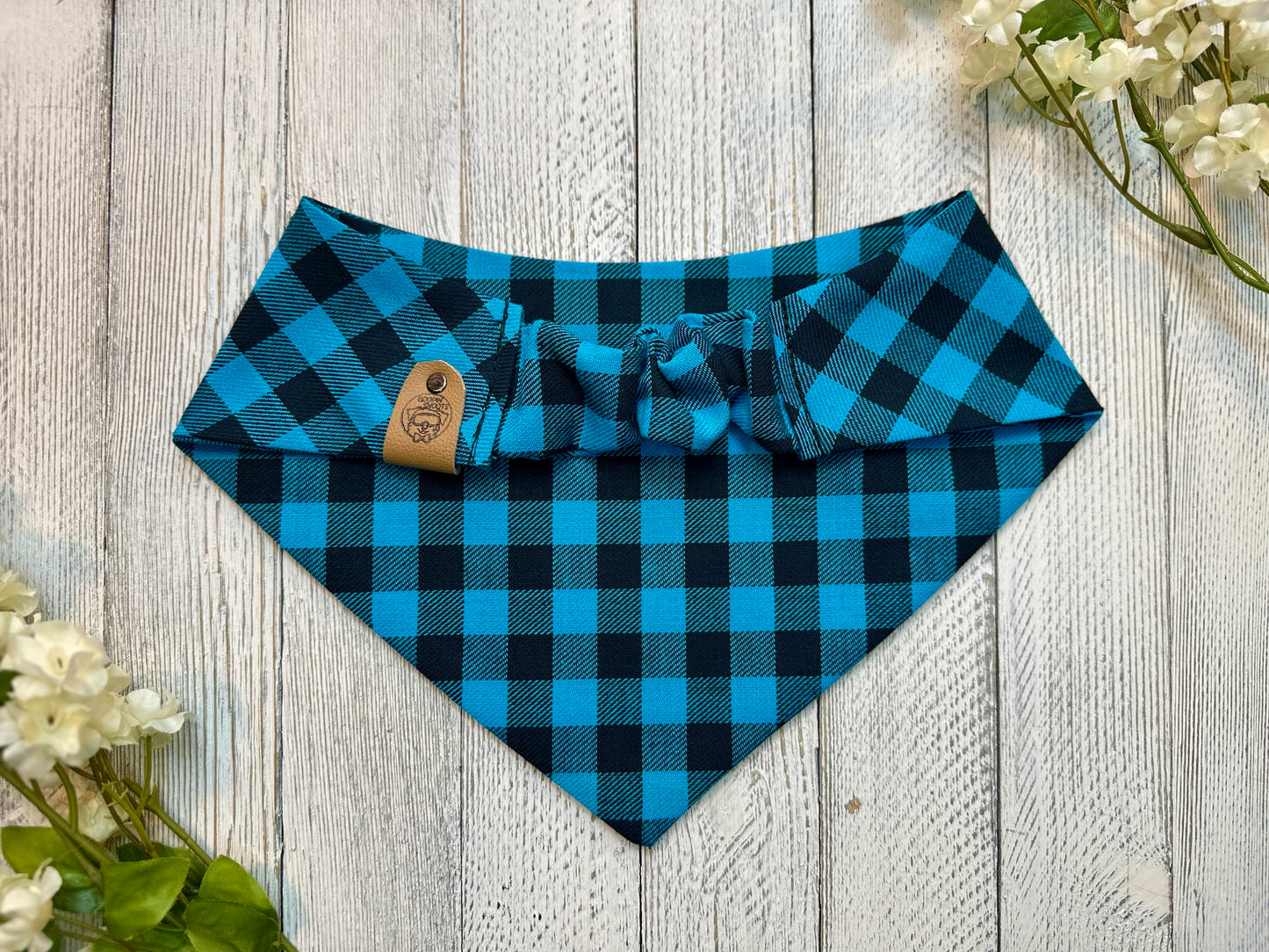 Picture of the backside of a pet bandana showing the scrunchie neckline. Displayed on a wooden surface with flowers for decoration. 