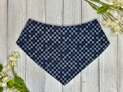 A pet bandana black and grey checkered pattern, displayed on a wooden surface with flowers for decoration. 