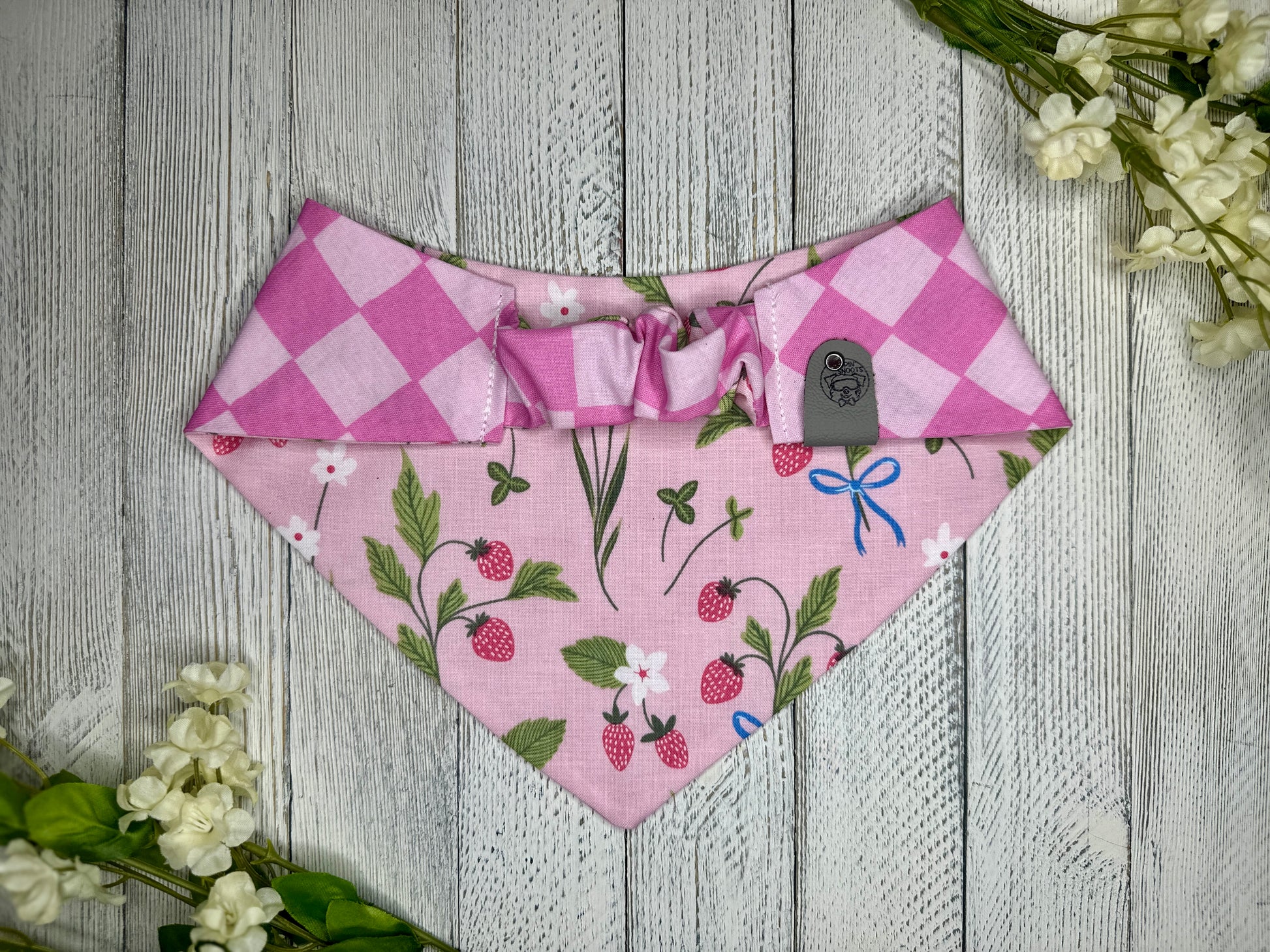 Picture of the backside of a pet bandana showing the scrunchie neckline. Displayed on a wooden surface with flowers for decoration. 