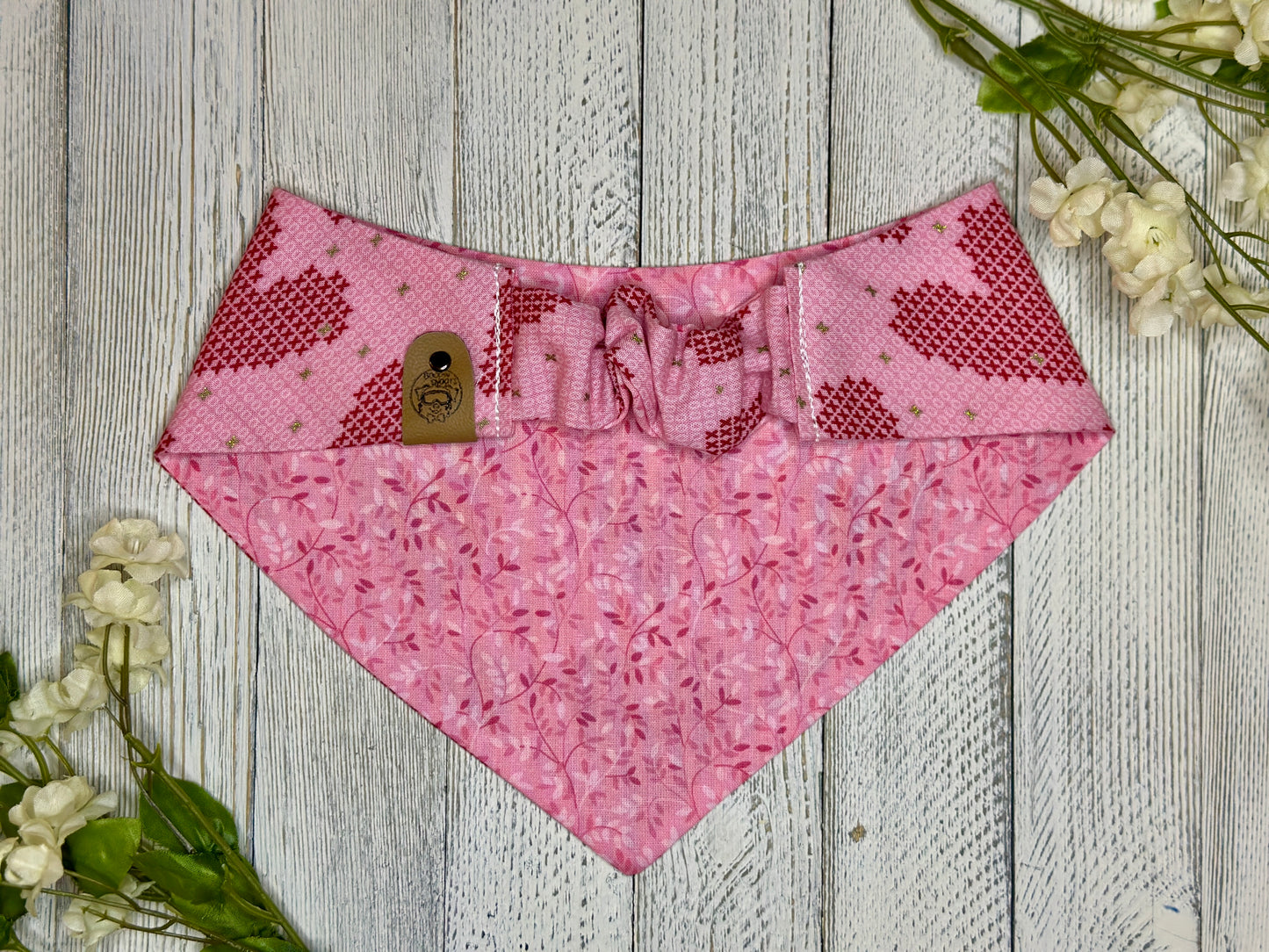 Picture of the backside of a pet bandana showing the scrunchie neckline. Displayed on a wooden surface with flowers for decoration. 