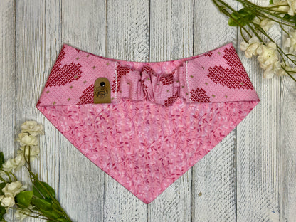 Picture of the backside of a pet bandana showing the scrunchie neckline. Displayed on a wooden surface with flowers for decoration. 