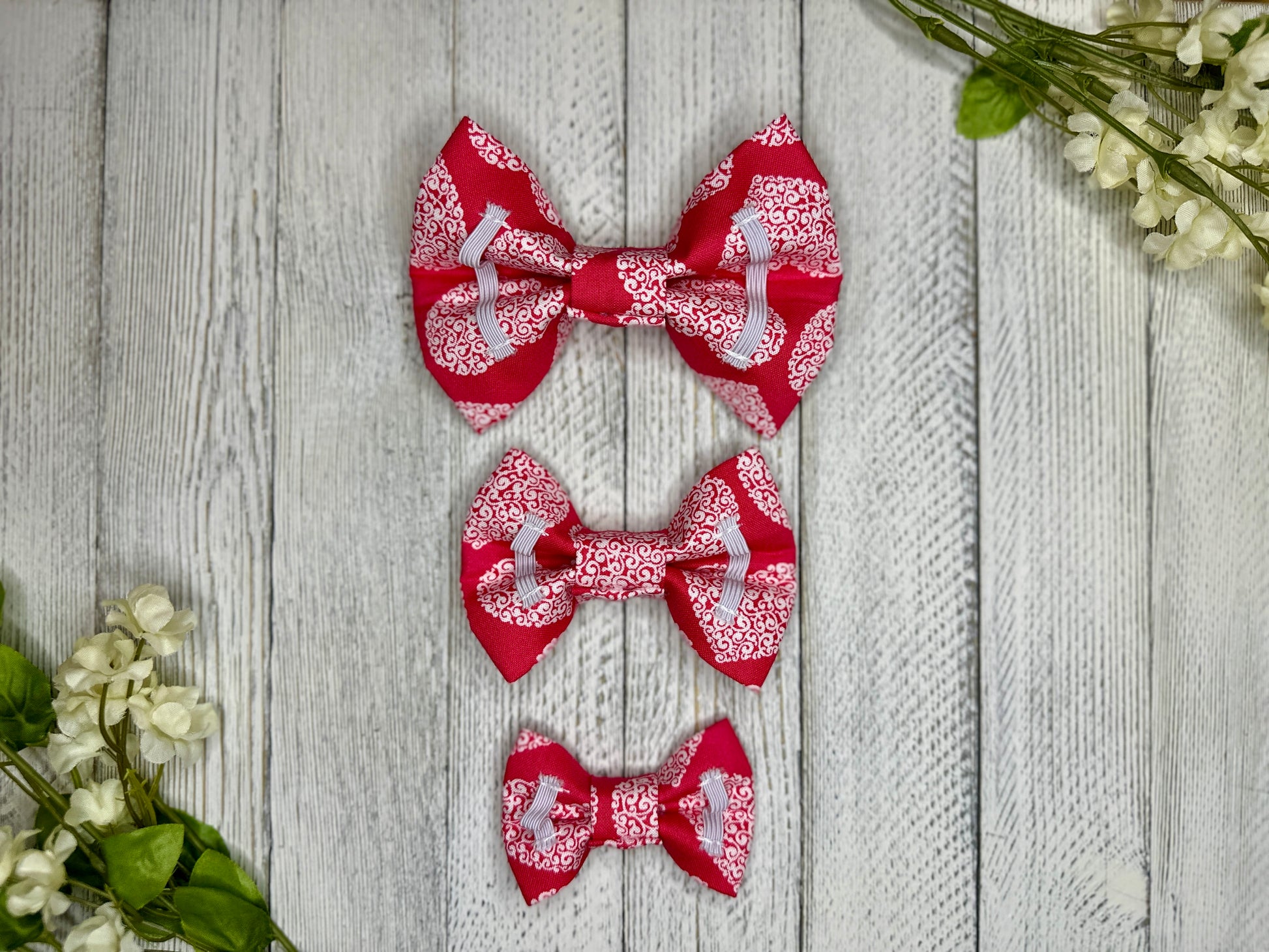 Picture of the backside of pet bow ties showing the elastic straps that fit around a collar. Displayed on a wooden surface with flowers for decoration. 
