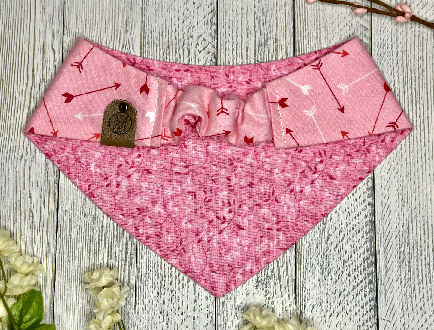 Picture of the backside of a pet bandana showing the scrunchie neckline. Displayed on a wooden surface with flowers for decoration. 