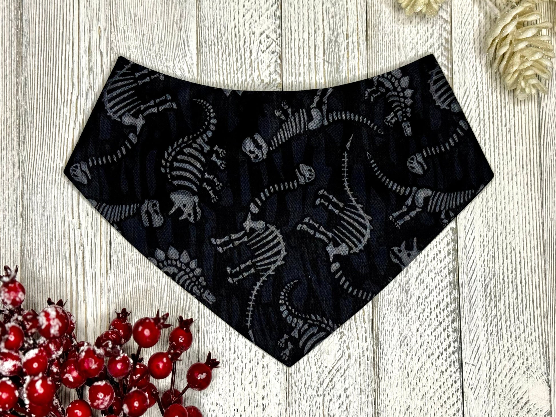 A black pet bandana with dinosaur fossils pattern, displayed on a wooden surface.