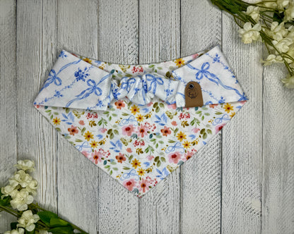 Picture of the backside of a pet bandana showing the scrunchie neckline. Displayed on a wooden surface with flowers for decoration. 