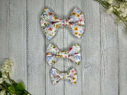 Picture of the backside of pet bow ties showing the elastic straps that fit around a collar. Displayed on a wooden surface with flowers for decoration. 