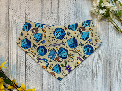 Pet bandana with blue dice and gaming-themed design on a wooden surface with flowers.