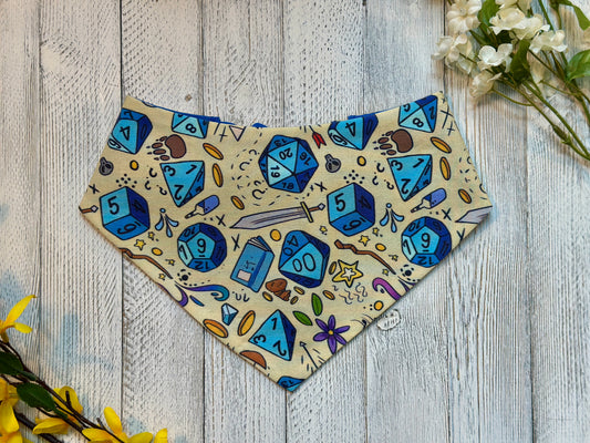 Pet bandana with blue dice and gaming-themed design on a wooden surface with flowers.