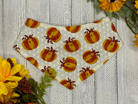 A bandana with a golden leaves pattern displayed on a wooden surface surrounded by flowers.