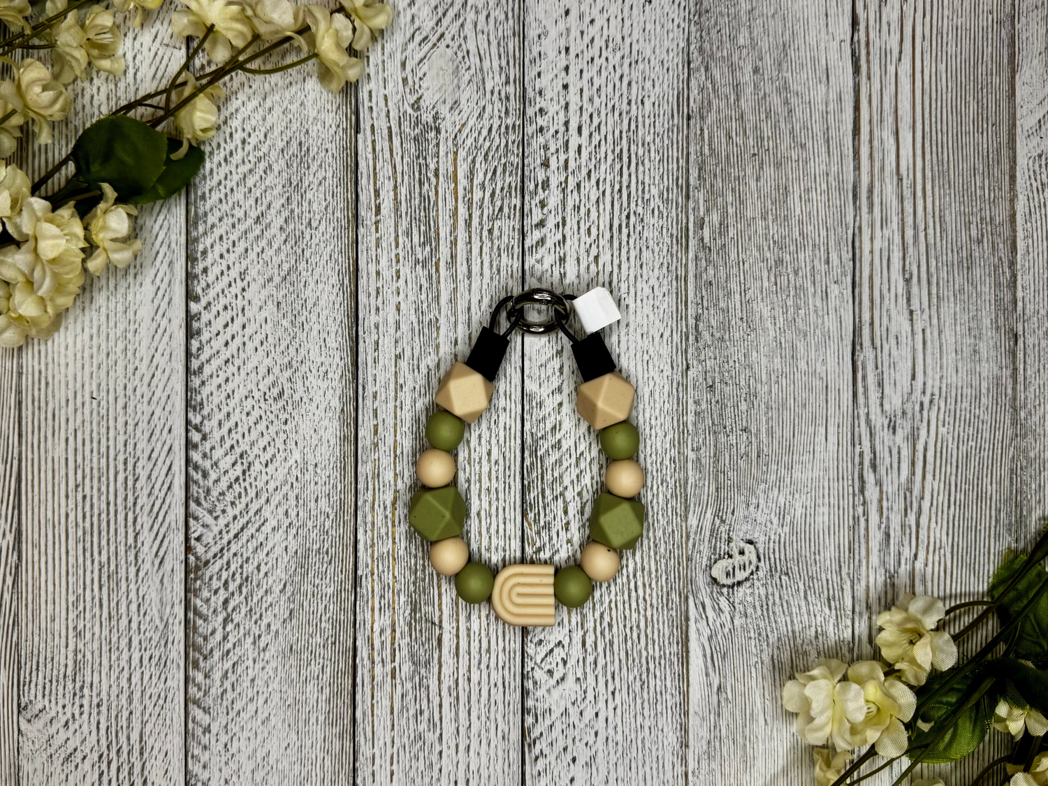 Beaded dog necklace with tan and olive tones including a rainbow. Displayed on a wooden surface with flowers for decoration