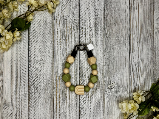 Beaded dog necklace with tan and olive tones including a rainbow. Displayed on a wooden surface with flowers for decoration