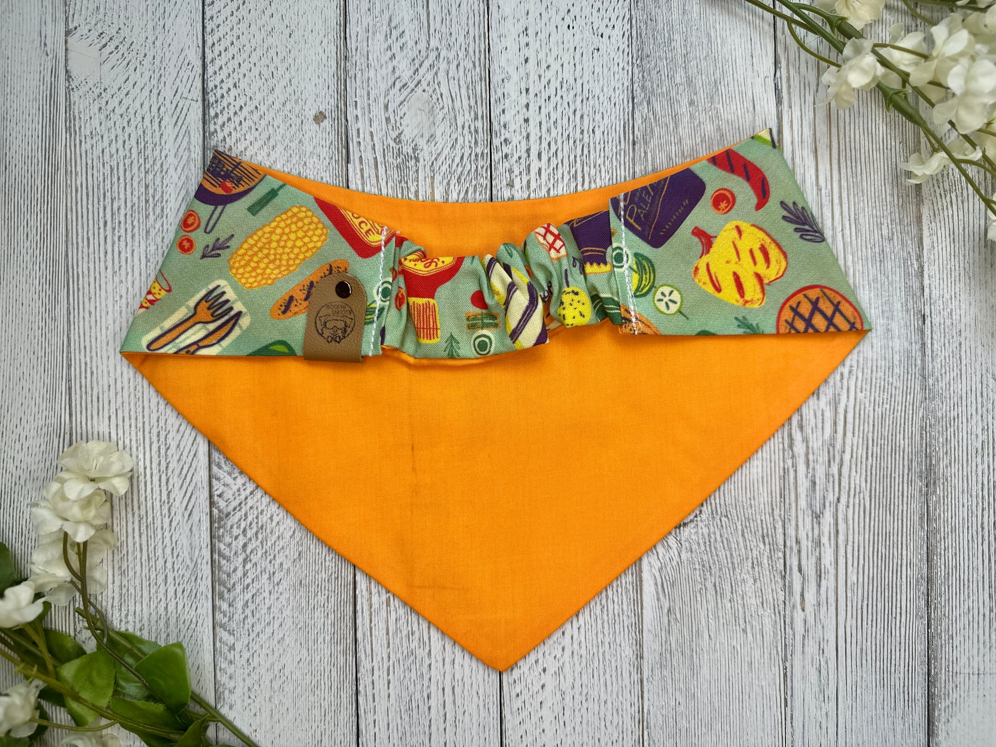 Picture of the backside of a pet bandana showing the scrunchie neckline. Displayed on a wooden surface with flowers for decoration. 