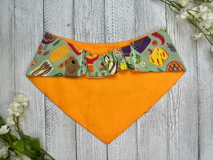 Picture of the backside of a pet bandana showing the scrunchie neckline. Displayed on a wooden surface with flowers for decoration. 