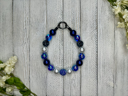 Beaded pet necklace with a navy blue pattern including sparkles. Displayed on a wooden surface with flowers for decoration.