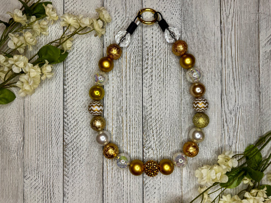 Beaded dog necklace with a gold pattern including zig zags. Displayed on a wooden surface with flowers for decoration.