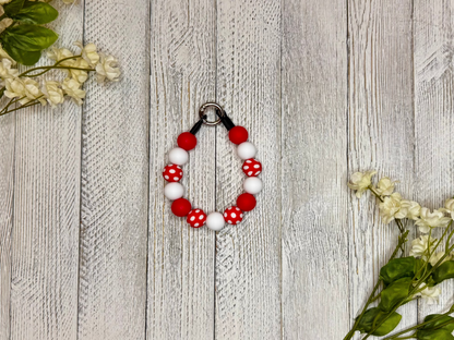 Beaded dog necklace with red and white pattern including polka dots. Displayed on a wooden surface with flowers for decoration