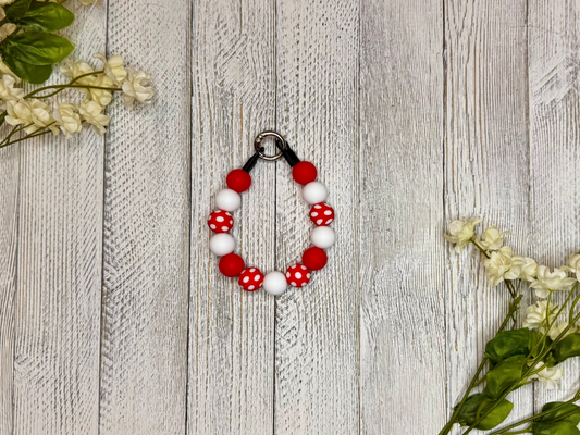Beaded dog necklace with red and white pattern including polka dots. Displayed on a wooden surface with flowers for decoration