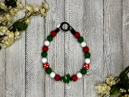 Beaded dog necklace with a red, green, and white pattern including a Christmas tree. Displayed on a wooden surface with flowers for decoration.