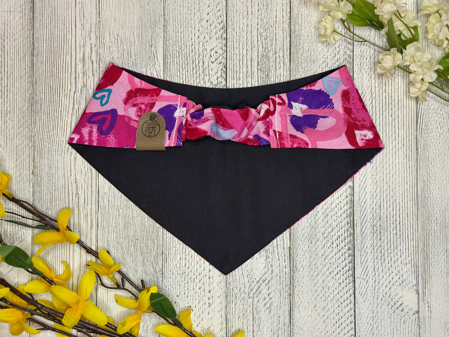 Picture of the backside of a pet bandana showing the scrunchie neckline. Displayed on a wooden surface with flowers for decoration. 