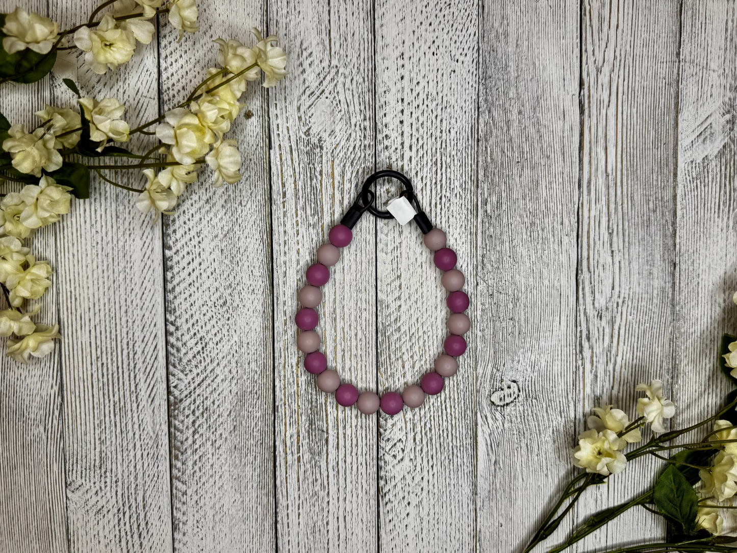 Beaded dog necklace with light and dark mauve pattern. Displayed on a wooden surface with flowers for decoration