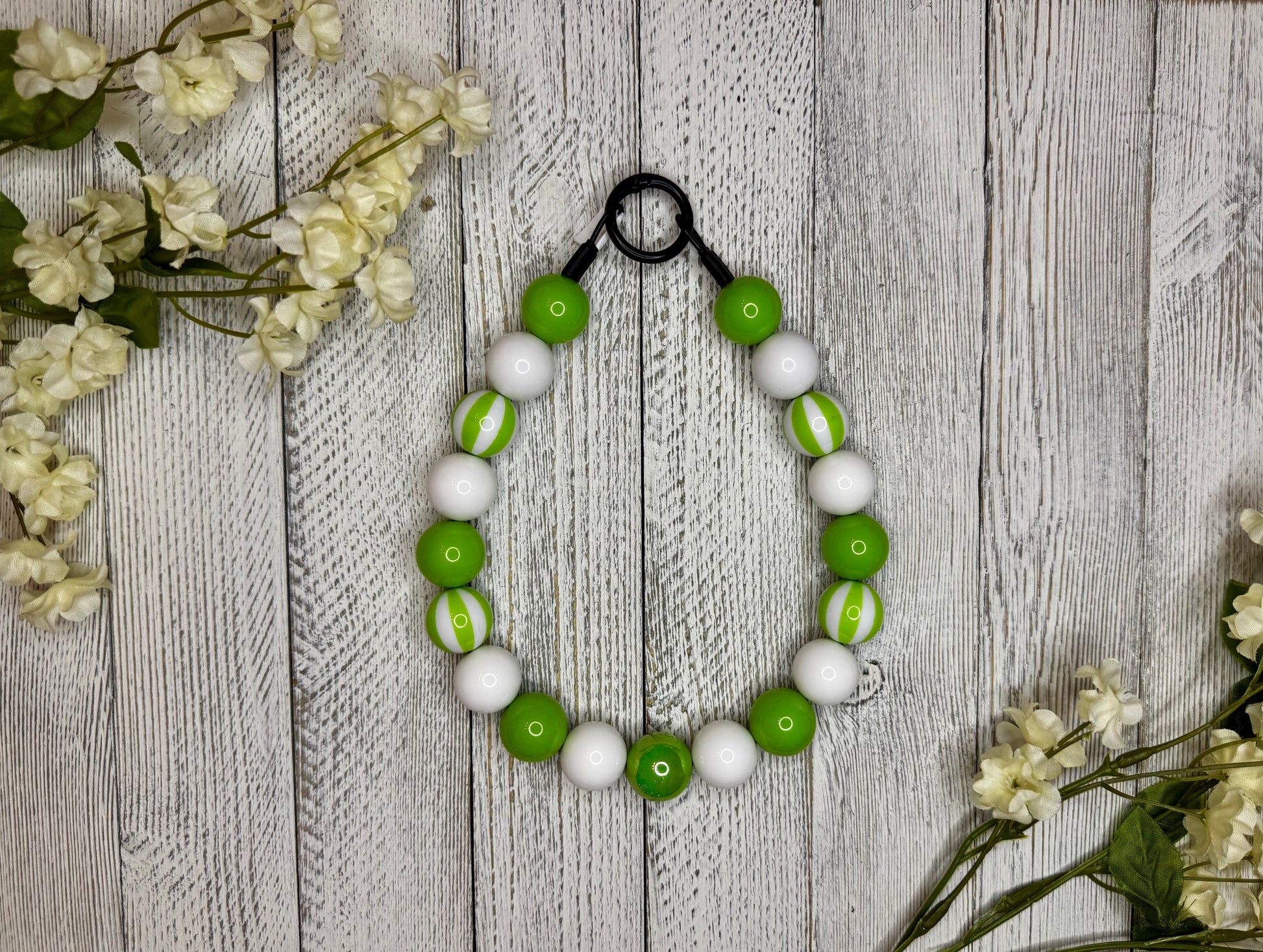Beaded dog necklace with a lime green and white pattern including stripes. Displayed on a wooden surface with flowers for decoration.