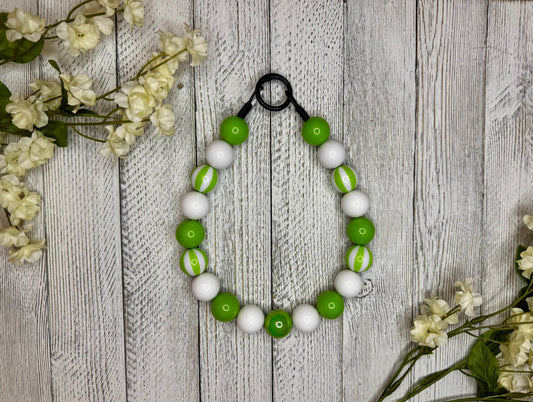 Beaded dog necklace with a lime green and white pattern including stripes. Displayed on a wooden surface with flowers for decoration.