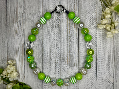 Beaded pet necklace with a lime and white pattern, including stripes. Displayed on a wooden surface with flowers for decoration. 
